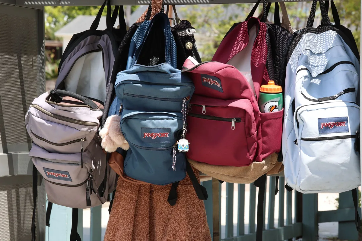 A collection of colorful backpacks hanging outside on a sunny day, representing back-to-school sourcing.
